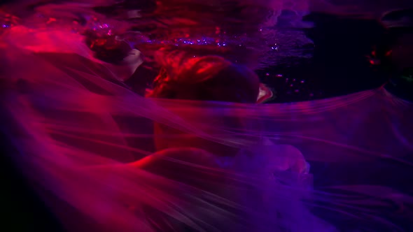 the Woman Whirls and Wraps Herself in a Translucent Cloth in the Dark Water. Purple Contour Light