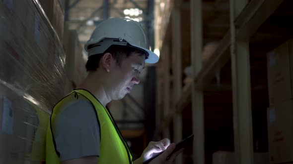 Young Warehouse Worker Man with Safety Hard Hat Checking Order Details with Tablet at Inventory Room