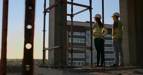 Two Chief Engineer with a Drawing in Hand Looking at the Construction Site