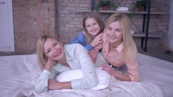 Family Leisure with Mother, Happy Mama Enjoys Relaxing with Beautiful Daughters Lying on Bed While