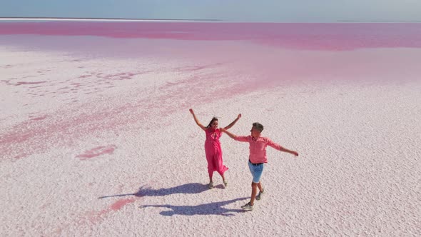 Aerial Drone Footage of Happy Joyful Couple Having Fun and Walking on Bright Colorful Pink Water of