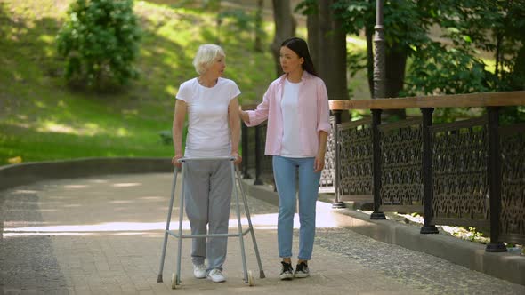 Woman Supporting Disabled Elderly Grandmother, Walking in Hospital Park, Illness