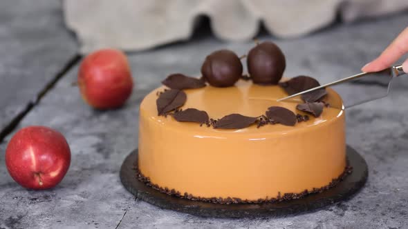 Female Hands Cutting a Caramel Apple Mousse Cake with Mirror Glaze. Autumn cake.French Food.