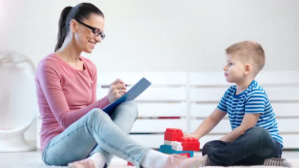 Smiling Female Kid Psychologist Watching and Taking Notes During Psychology Testing