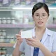 Asian female pharmacist explaining the medicinal properties on the pillbox to a patient or customer - VideoHive Item for Sale