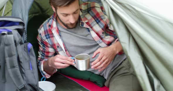 Close Up of Young Man Drinking Hot Coffee After Hiking. Beautiful Man Relaxing in a Tent. Camping