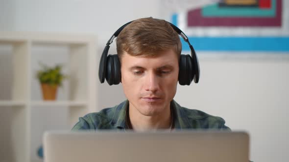 Young Concentrated Man Using Laptop and Headphones at Home