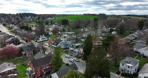 American town in bright sunny light reveals homes along street. Colorful aerial spring establishing