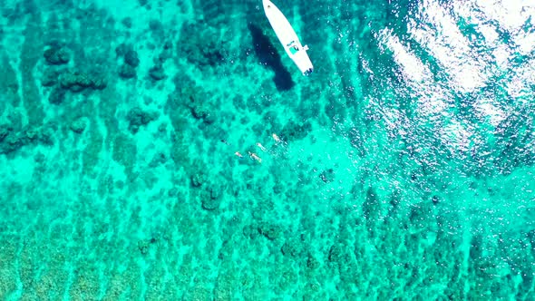 White boat anchoring on turquoise lagoon, people swim and snorkel on crystal clear water, watching b