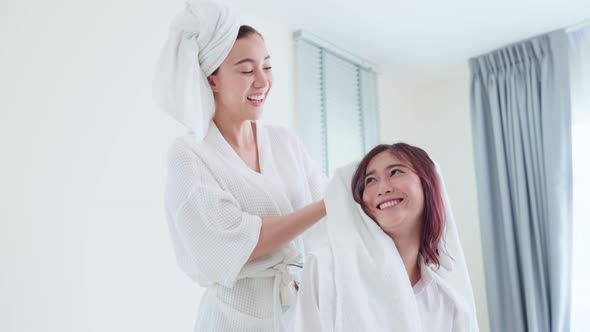 Asian beautiful lesbian couple drying girlfriend's hair after shower on bed in bedroom in house.