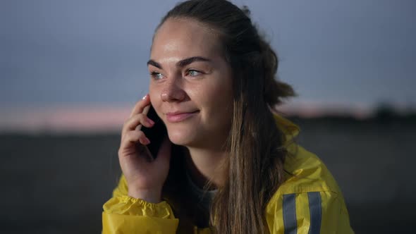 Young Happy Woman Talking on Phone Sitting at Dusk on Field Outdoors