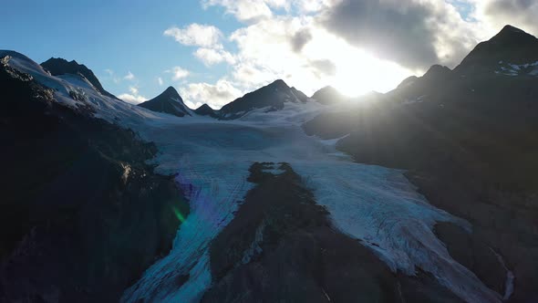 Aerial closeup sliding near ice-capped mountain slope against shining sun in summer Alaska