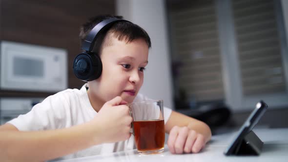 Boy looking at tablet. Cute boy drinking tea for breakfast at home while watching cartoon on tablet