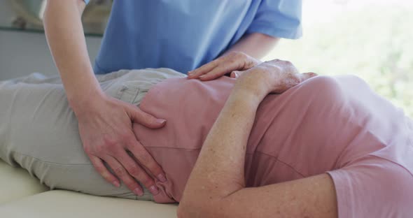 Female health worker massaging hips of senior woman at home