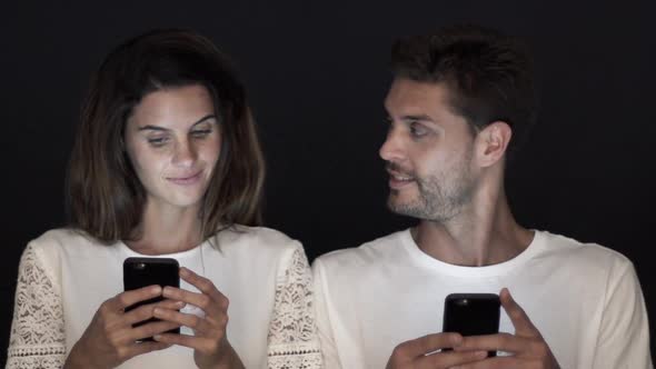 Couple smiling at each other while relaxing with smartphones