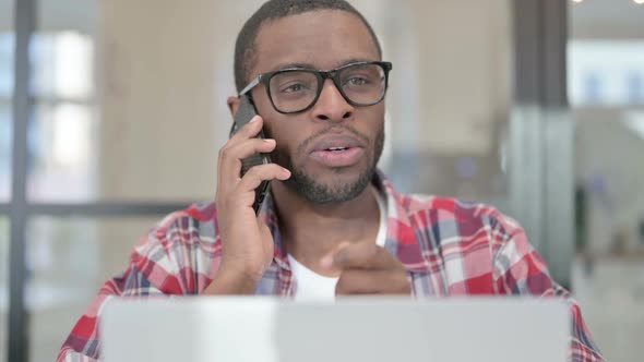 Close Up of African Man with Laptop Talking on Smartphone