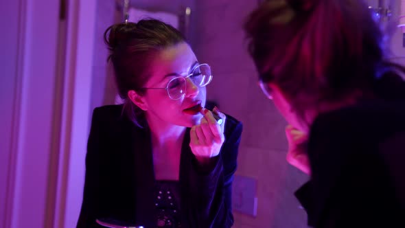 Portrait of a Sexy Brunette Woman in Round Glasses Posing Standing in Front of a Mirror Looking at