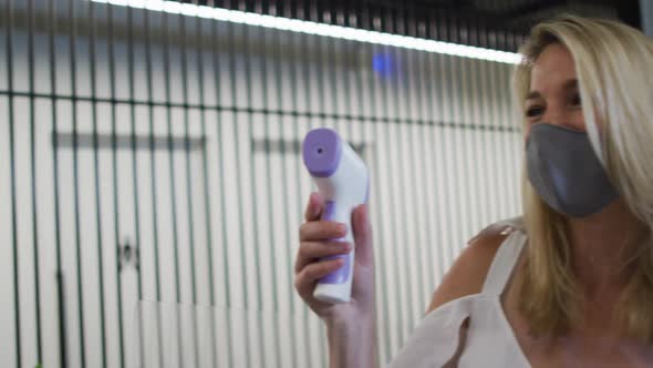 Caucasian businesswoman wearing face mask checking coworkers temperature