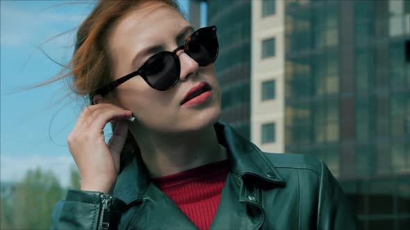 Young Woman Wears Headphones and Turns on Music in a Mobile Phone on the Street, While Walking in an