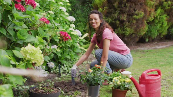 Happy biracial woman gardening, planting flowers