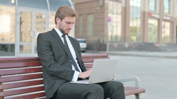 Businessman with Laptop Showing Thumbs Up Sign While Sitting Outdoor on Bench