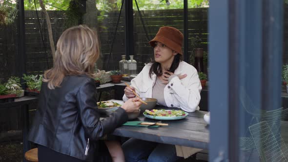 Young Woman Sharing with Her Friend Over Lunch in Hipster Café