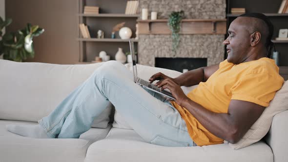 Senior African Writer Freelancer Businessman Buyer Lying on Sofa at Home Feel Inspiration Typing