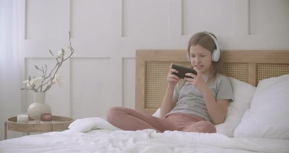 Children and Internet Games, Little Girl Is Playing By Smartphone Sitting in Bedroom, Internet