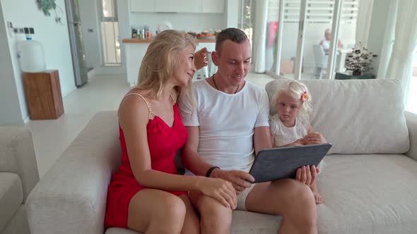 Couple with Daughter Sitting on the Couch and Using a Tablet