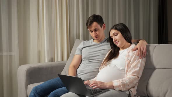 Married Couple Does Online Shopping for Baby Hugging on Sofa