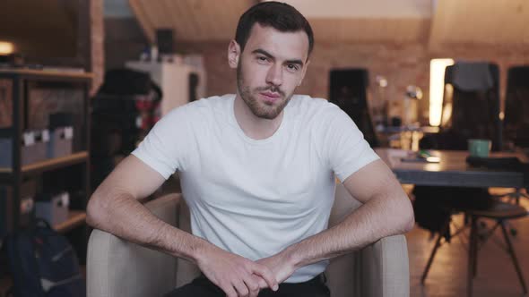 A Young Attractive Man Sits in a Chair in the Office and Looks Into the Camera