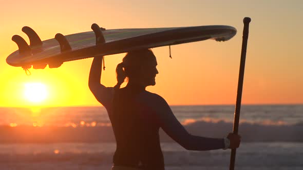 A silhouetted portrait of woman sup stand-up paddleboard surfing at the beach at sunset