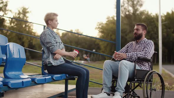 Disabled Person Man in Wheelchair Dating in Park and Drinks Coffee with Woman Side View