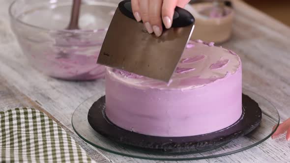 The process of decorating a cake with purple cream cover. 