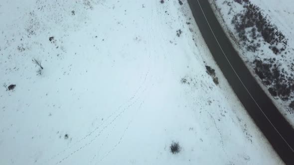 Drone flying over a small rural road with the ground covered by snow. Aerial view of snowy rural lan