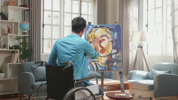 Hind View Of An Asian Artist Man In Wheelchair Holding Paintbrush Mixed Colour And Painting