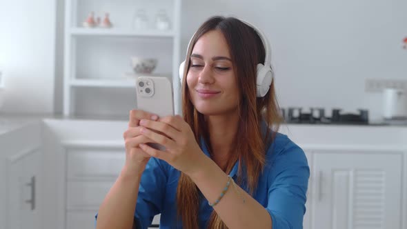 Close Up Woman in Darkblue Shirrt in Headphones Listening Music in Kitchen Background