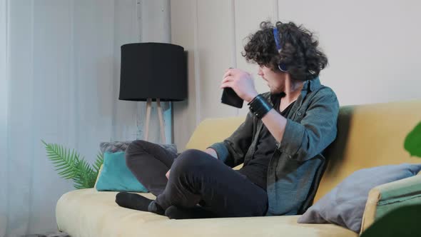 Curly Haired Young Man on the Couch Listening Music with Headphones