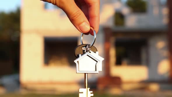 Hand with the key to the future house on the background of a construction site and walls