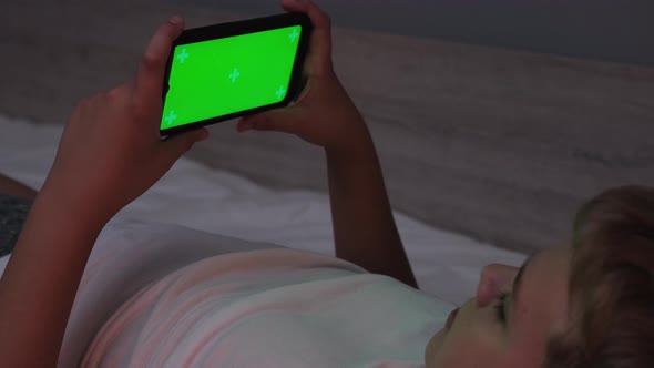 Male Teenager Lying on His Bed While Scrolling Through Social Media on His Phone