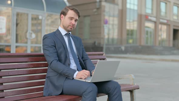 Businessman with Laptop Looking at Camera while Sitting Outdoor on Bench