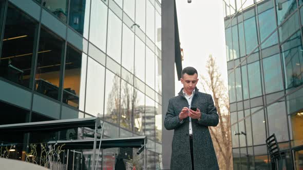 Businessman Is Using Smartphone App and Walking Near Modern Office Building