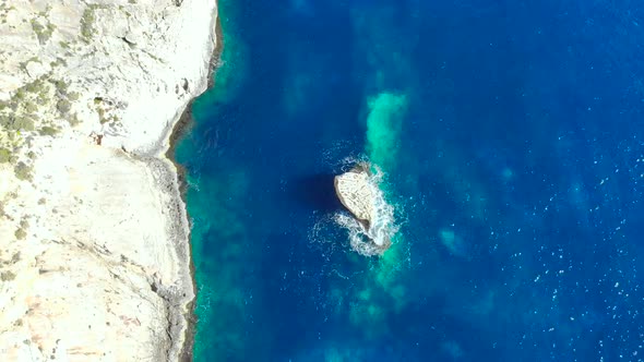 Drone shot over rocks and Cliffs with wave hitting a small rock in the Mediterranean sea of Malta 3