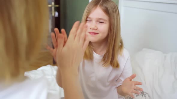 Mom and Daughter Play Palms on the Bed in the Bedroom