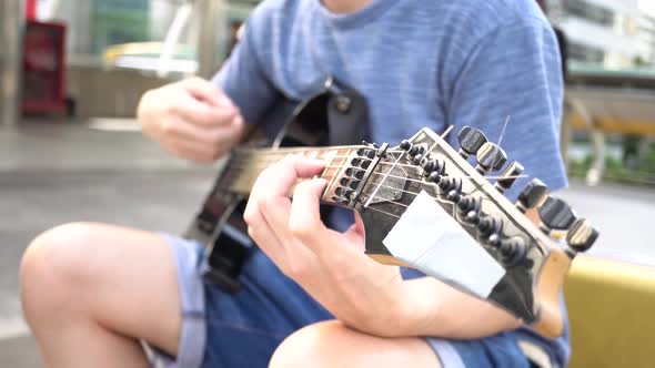 Street Musician Strumming Guitar on the Street Outdoors While Passerby Walking By