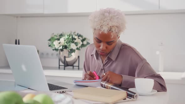 Young African American Business Woman Looking in Laptop and Makes Notes