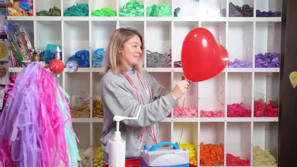 a Woman Ties a Ribbon on Inflated Helium Red Balloon in the Shape of a Heart