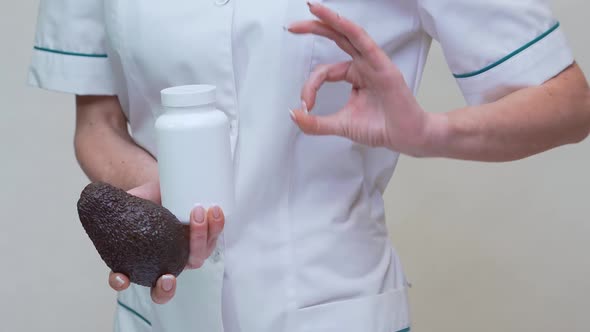 Nutritionist Doctor Holding Organic Avocado Fruit and Jar of Medicine or Vitamin or Omega 3 Capsules