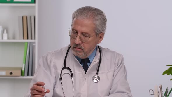Aged Male Doctor in White Medical Coat Carefully Examines the Vaccine Vials
