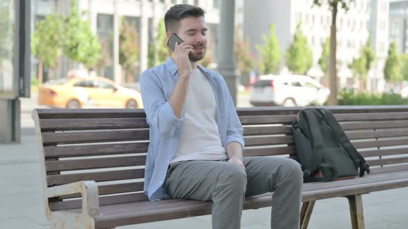 Young Man Talking on Phone While Sitting on Bench